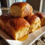 A stack of freshly baked, golden brown Texas Roadhouse Rolls glistening with honey butter glaze.