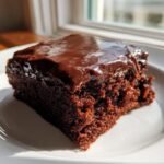Close-up of a moist, dark chocolate slice of Texas Sheet Cake topped with glossy, melted chocolate frosting.