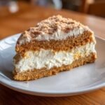 A delicious slice of Vanilla Wafer Cake showing layers of golden cake and thick white cream filling, topped with crumbs.