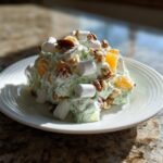 A scoop of bright green Watergate Salad topped with mini marshmallows, pecans, and mandarin oranges on a white plate.