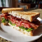 A close-up of a delicious BLT Sandwich cut in half, showing crispy bacon, thick tomato slices, lettuce, and mayo on toasted white bread.