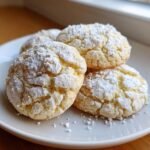 A stack of soft Amish Buttermilk Cookies generously dusted with cracked powdered sugar on a white plate.