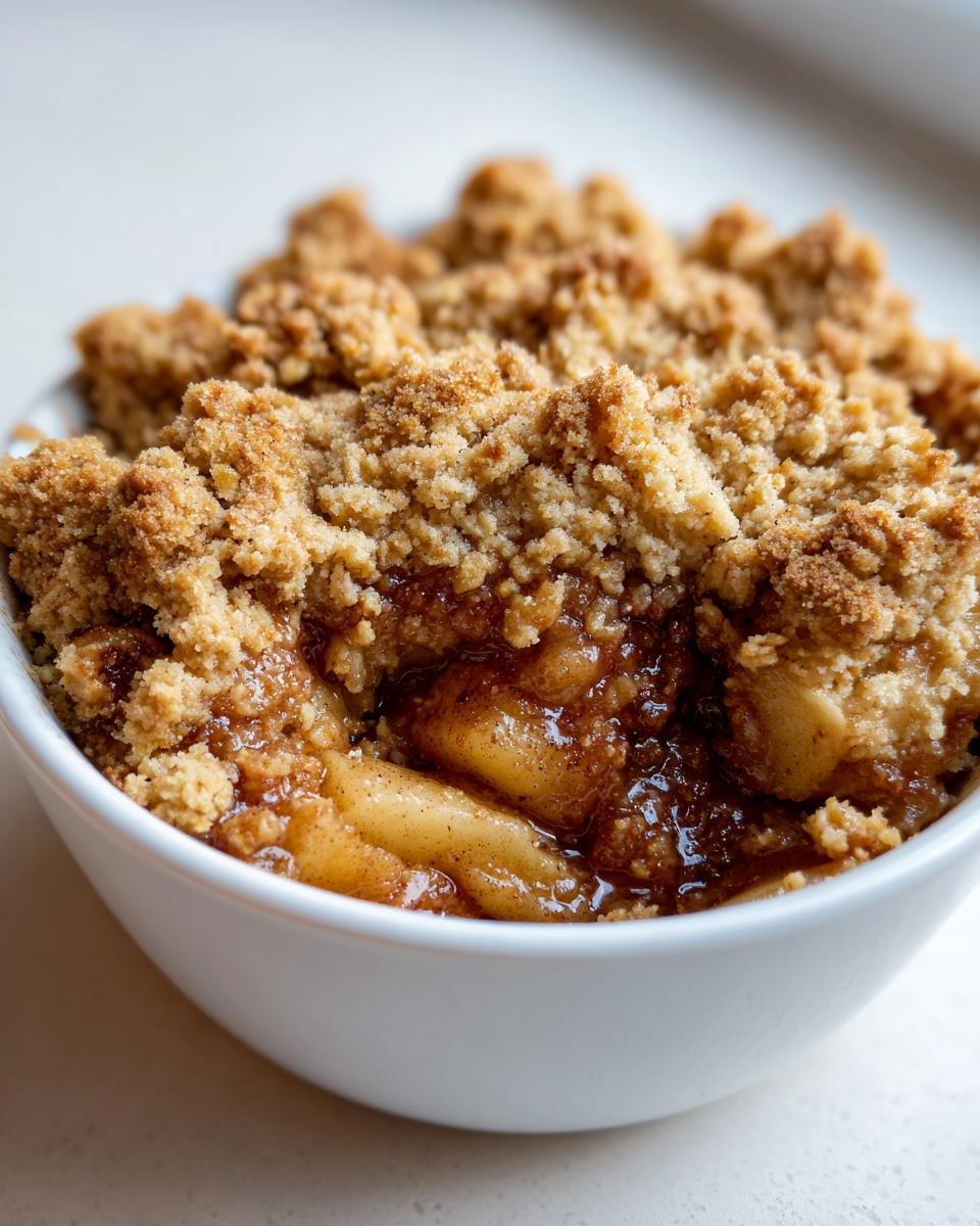 A close-up view of a serving of warm Apple Crisp with a thick, crumbly topping and gooey spiced apples underneath.