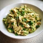 A close-up view of creamy, shredded Avocado Chicken Salad garnished with fresh cilantro in a white bowl.