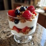 A close-up view of layered Yogurt Parfaits in a glass, featuring yogurt, granola, strawberries, blueberries, and raspberries.