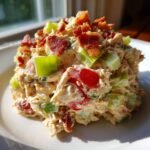 A mound of creamy BLT Chicken Salad featuring shredded chicken, red tomatoes, green celery, and topped with crispy bacon pieces.