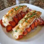 Two succulent, split broiled lobster tails seasoned with herbs and butter on a white plate.