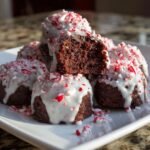 A stack of rich, dark Candy Cane Brownie Bombs drizzled with white glaze and topped with crushed peppermint candy.