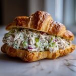 A delicious Chicken Salad Croissant Sandwich overflowing with creamy chicken salad, celery, and red onion.