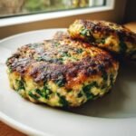 Close-up of two golden-brown, pan-seared Chicken Spinach Burgers showing visible green spinach flecks.