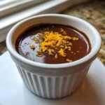 Close-up of a rich Chocolate Orange Posset dessert topped with bright orange zest in a white ramekin.