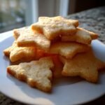 A stack of golden, star-shaped Christmas Butter Cookies sprinkled with sugar on a white plate.
