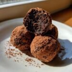 A stack of rich, dark Christmas Cake Truffles heavily dusted with cocoa powder, one cut open.