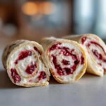 Close-up of sliced Cranberry Roll Ups showing a swirl of white cream cheese filling and dark red cranberry sauce inside a tortilla.