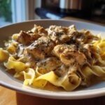 Close-up of creamy Chicken Stroganoff with chunks of chicken and herbs over wide egg noodles.