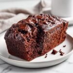 A rich, dark slice of Double Chocolate Banana Bread topped with melted chocolate chips on a white plate.