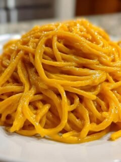 A close-up of a mound of spaghetti coated in a rich, orange Butternut Squash Pasta sauce, served on a white plate.