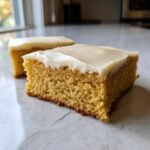 A close-up shot of a thick, golden square of Frosted Sugar Cookie Bars topped with creamy white frosting.