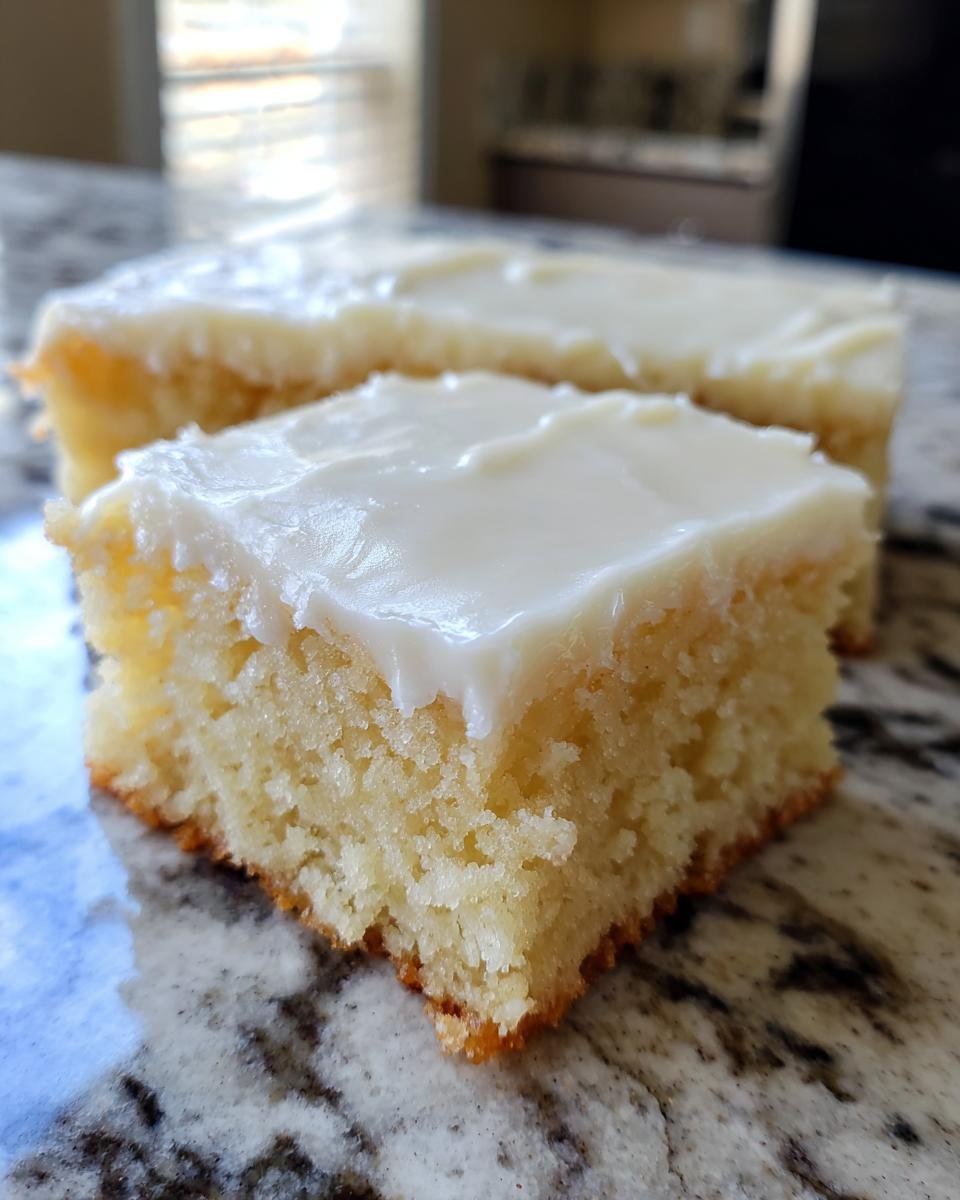 A close-up of a square slice of Frosted Sugar Cookie Bars with thick white frosting on a granite countertop.