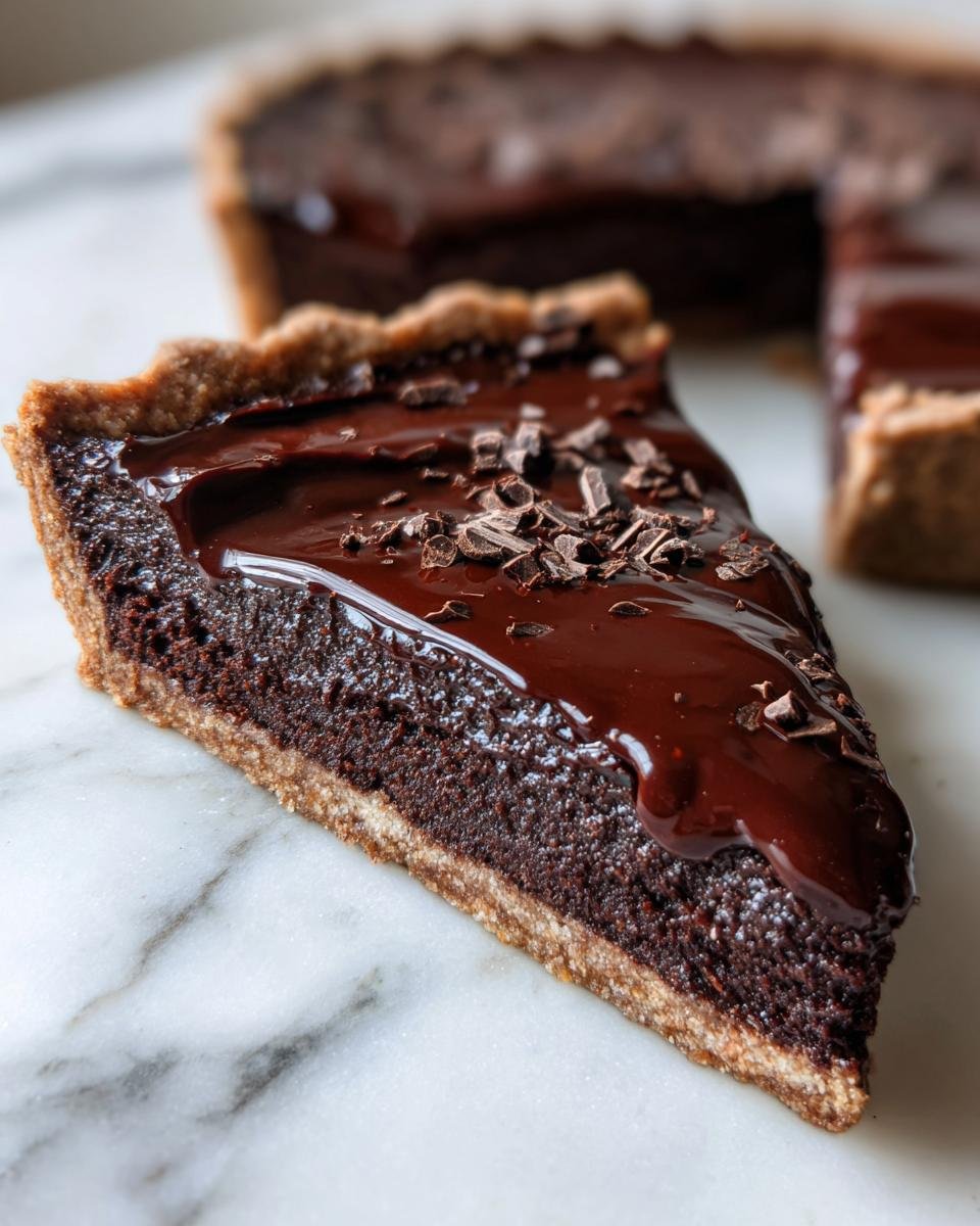 A close-up slice of Fudge Dessert Pizza with a thick, glossy chocolate ganache topping and chocolate shavings.
