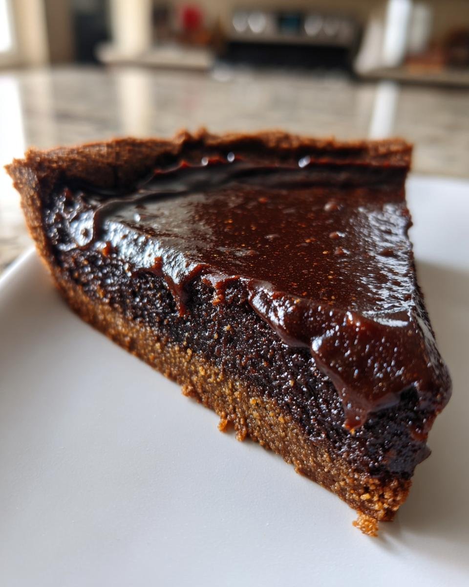Close-up of a decadent slice of Fudge Dessert Pizza showing a thick, glossy chocolate topping over a dense, dark base.