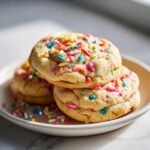 Close-up of three soft Funfetti Cake Mix Cookies stacked on a white plate, covered in colorful sprinkles.