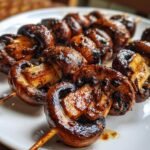 Close-up of perfectly charred and glazed Grilled Mushroom Skewers resting on a white plate.