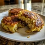Close-up of golden brown Cabbage Burgers on a white plate, one is broken open showing the shredded texture inside.