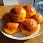 A stack of freshly baked, golden-orange Sweet Potato Rolls piled high on a white plate.