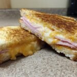 A perfectly grilled Ham And Cheese Sandwich cut diagonally, showing melted cheddar cheese and layers of ham.