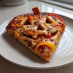 A slice of Jack O Lantern Pizza featuring a carved bell pepper face design, topped with melted cheese.