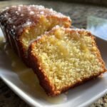 A close-up of a moist slice of Lemon Drizzle Cake topped with sugary glaze and extra lemon syrup.