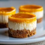 Three delicious Mini Orange Cheesecakes featuring a graham cracker crust, creamy filling, and bright orange topping.
