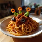 A plate of Monster Spaghetti featuring bolognese sauce, two black olive eyes, and three carrot-topped green pepper antennae.