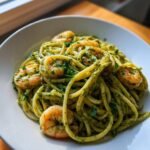 A close-up shot of delicious Pesto Shrimp Pasta tossed in vibrant green pesto sauce, served in a white bowl.