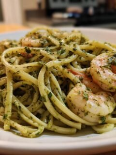 A close-up of creamy Pesto Shrimp Pasta featuring thick linguine coated in green pesto sauce and topped with pink cooked shrimp.