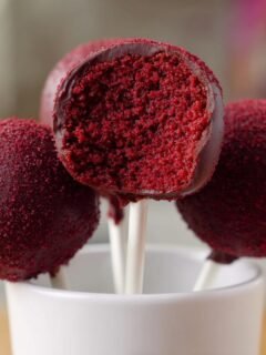 Close-up of three Red Velvet Cake Pops, one cut open revealing the rich red interior, displayed in a white mug.