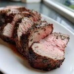 Close-up of medium-rare slices of seasoned Beef Tenderloin Roast on a white platter.