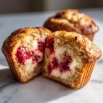 A Strawberry Cream Cheese Muffin cut in half showing the bright red fruit and creamy white filling.