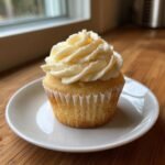 A single vanilla Keto Cupcakes topped with swirled cream cheese frosting, sitting on a white plate.