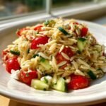 Close-up of a vibrant Orzo Pasta Salad featuring cherry tomatoes, cucumber chunks, and feta cheese.