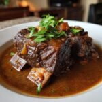 Close-up of tender Beef Short Ribs braised in a rich, dark sauce and garnished with fresh parsley.