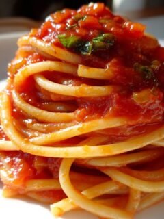 A perfectly twirled mound of spaghetti coated in rich, chunky Tomato Pasta sauce, garnished with fresh basil.