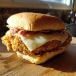 Close-up of a golden, crispy Chicken Cordon Bleu Sandwich featuring melted Swiss cheese and ham on a soft bun.