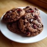 A stack of four rich, dark Chocolate Cherry Cookies featuring visible chocolate chips and dried cherries on a white plate.