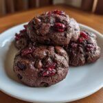 A stack of four fudgy Chocolate Cherry Cookies topped with dried cherries and chocolate chips on a white plate.