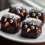 Four adorable chocolate-dipped Snowmen Truffles decorated with candy eyes, orange beaks, and pretzel arms.