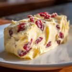 A rich block of homemade Cranberry Honey Butter studded with dried cranberries, resting on a white plate.