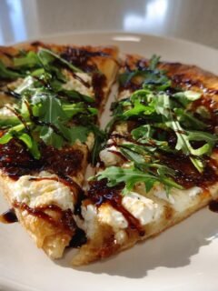 Two slices of Fig Jam Goat Cheese Pizza topped with creamy goat cheese, dark fig jam, fresh arugula, and balsamic glaze.