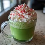A vibrant green Grinch Hot Chocolate topped with whipped cream and red sprinkles.